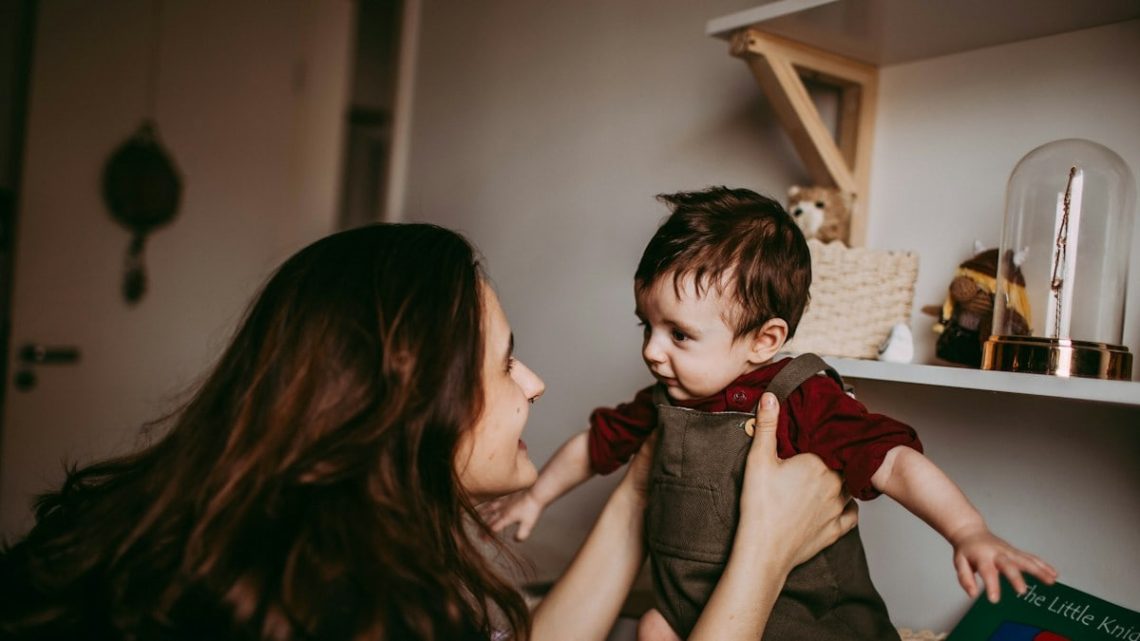 woman in red shirt carrying girl in gray sleeveless dress