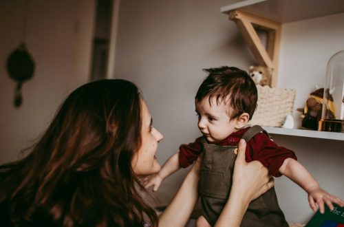 woman in red shirt carrying girl in gray sleeveless dress